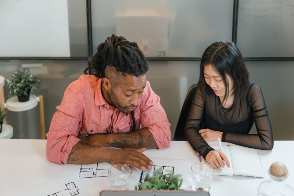 Two people discussing blueprints in an office setting, engaging in collaborative work.